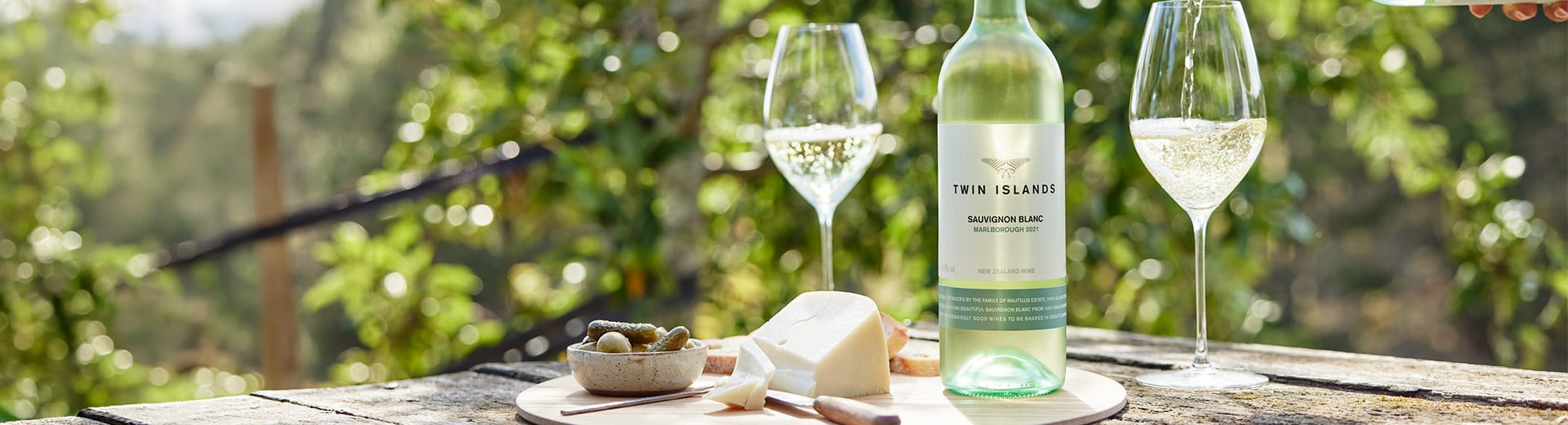 an image featuring a bottle of twin islands on an outdoor table, alongside a second bottle pouring into a wine glass